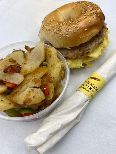 Boxed breakfast: hot egg sandwich on a bagel with home fries, packaged for one